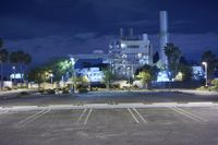 an industrial factory lit up at night with lights and parking lot in front of it