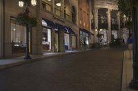 people walking down a city street at night time in front of store fronts and a street light