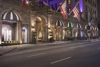 a hotel with multiple flags hanging from the front and outside windows at night time with cars driving down the street below