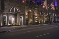 a hotel with multiple flags hanging from the front and outside windows at night time with cars driving down the street below