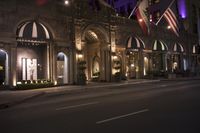 a hotel with multiple flags hanging from the front and outside windows at night time with cars driving down the street below