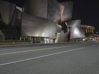 an outside shot of a building at night, with light pouring on it and yellow lines on the road