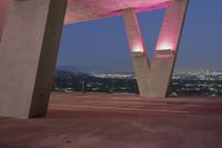 the pink light shines on the street below a tall concrete structure in the city