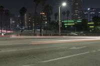 an empty street surrounded by palm trees and tall buildings at night with traffic coming to the lights