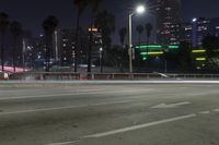 an empty street surrounded by palm trees and tall buildings at night with traffic coming to the lights