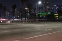 an empty street surrounded by palm trees and tall buildings at night with traffic coming to the lights