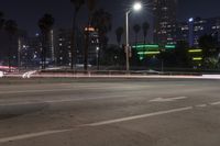 an empty street surrounded by palm trees and tall buildings at night with traffic coming to the lights