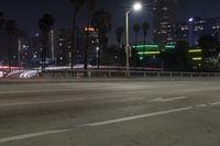 an empty street surrounded by palm trees and tall buildings at night with traffic coming to the lights