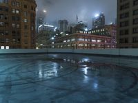 a wet roof at night next to tall buildings and skyscrapers with reflections in the puddle