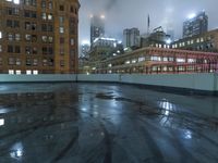 a wet roof at night next to tall buildings and skyscrapers with reflections in the puddle