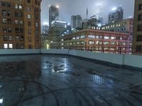 a wet roof at night next to tall buildings and skyscrapers with reflections in the puddle