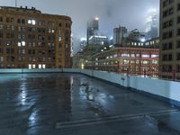 a wet roof at night next to tall buildings and skyscrapers with reflections in the puddle