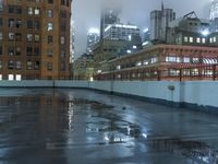 a wet roof at night next to tall buildings and skyscrapers with reflections in the puddle
