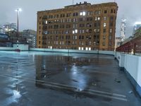 a wet roof at night next to tall buildings and skyscrapers with reflections in the puddle