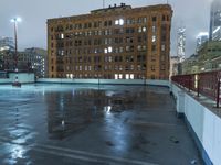 a wet roof at night next to tall buildings and skyscrapers with reflections in the puddle