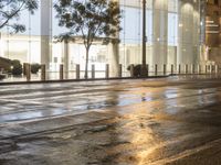 the sidewalk has some rain on it near some buildings at night with one pedestrian walking away