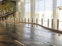 the sidewalk has some rain on it near some buildings at night with one pedestrian walking away
