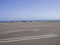 an empty parking lot with a few cars parked on it and ocean in the background