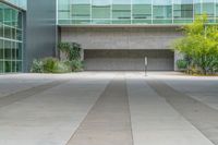 an outside courtyard with an empty bench and green plants on it in front of a glass building