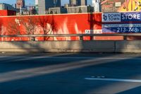 a red wall in the middle of an empty street with a city skyline behind it