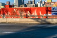 a red wall in the middle of an empty street with a city skyline behind it