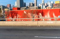 a red wall in the middle of an empty street with a city skyline behind it