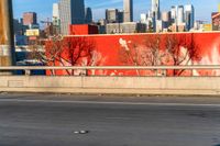 a red wall in the middle of an empty street with a city skyline behind it