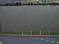 an empty parking lot and a fence behind it with some building glass in the background