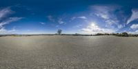 a large open field with a sky and clouds in the background and a tree on the ground near by