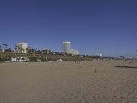 a group of people on a beach next to the ocean and a resort on the horizon