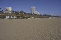 a group of people on a beach next to the ocean and a resort on the horizon