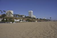 a group of people on a beach next to the ocean and a resort on the horizon