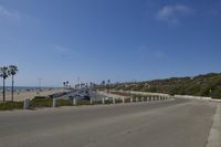 there is an empty street on the side of the beach road at the beach, and there are palm trees near the sea, on a hill, a sign showing where cars and other parked, are at the same point a sand area with a beach,