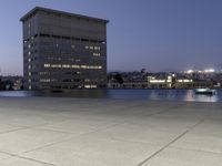 the walkway at the park leads to a lake and buildings in the background as evening falls