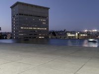 the walkway at the park leads to a lake and buildings in the background as evening falls