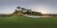 a 360 lens photo of a slope in a park with mountains behind it, and the sun setting on the horizon