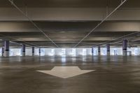 an empty parking garage with directional arrows in the space around the space and in the center, to indicate that is not a parking spot for cars