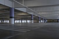 large empty parking area with poles and a skylight above it in a building with concrete floors, two long pillars, and no people