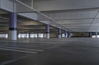 large empty parking area with poles and a skylight above it in a building with concrete floors, two long pillars, and no people