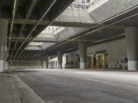 empty parking garage with concrete floors next to the curb walk under a bridge over a busy street