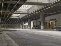 empty parking garage with concrete floors next to the curb walk under a bridge over a busy street