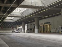 empty parking garage with concrete floors next to the curb walk under a bridge over a busy street