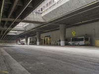 empty parking garage with concrete floors next to the curb walk under a bridge over a busy street