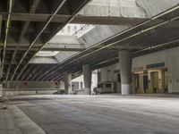 empty parking garage with concrete floors next to the curb walk under a bridge over a busy street