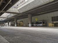 empty parking garage with concrete floors next to the curb walk under a bridge over a busy street