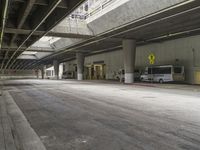 empty parking garage with concrete floors next to the curb walk under a bridge over a busy street