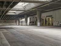 empty parking garage with concrete floors next to the curb walk under a bridge over a busy street