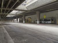 empty parking garage with concrete floors next to the curb walk under a bridge over a busy street