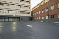 the empty parking lot is next to the large building which the apartments are located behind