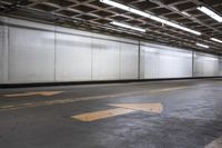 an empty concrete parking garage with no doors and a yellow arrow painted on the floor